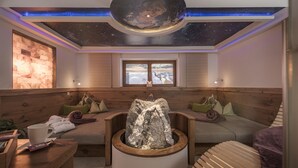 Un spa con un banco de madera, un elemento decorativo de piedra, una ventana con vista nevada y un techo estrellado.