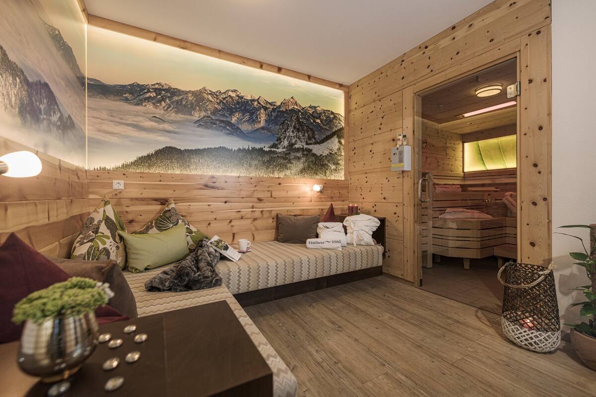 Une pièce chaleureuse avec un lit, un mur en bois, une fresque représentant des montagnes et une petite table sur laquelle est posée une plante.
