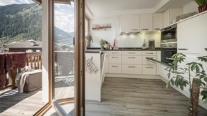 Una cocina moderna con armarios blancos, encimera de madera y vistas a un paisaje montañoso a través de una puerta corrediza de vidrio.