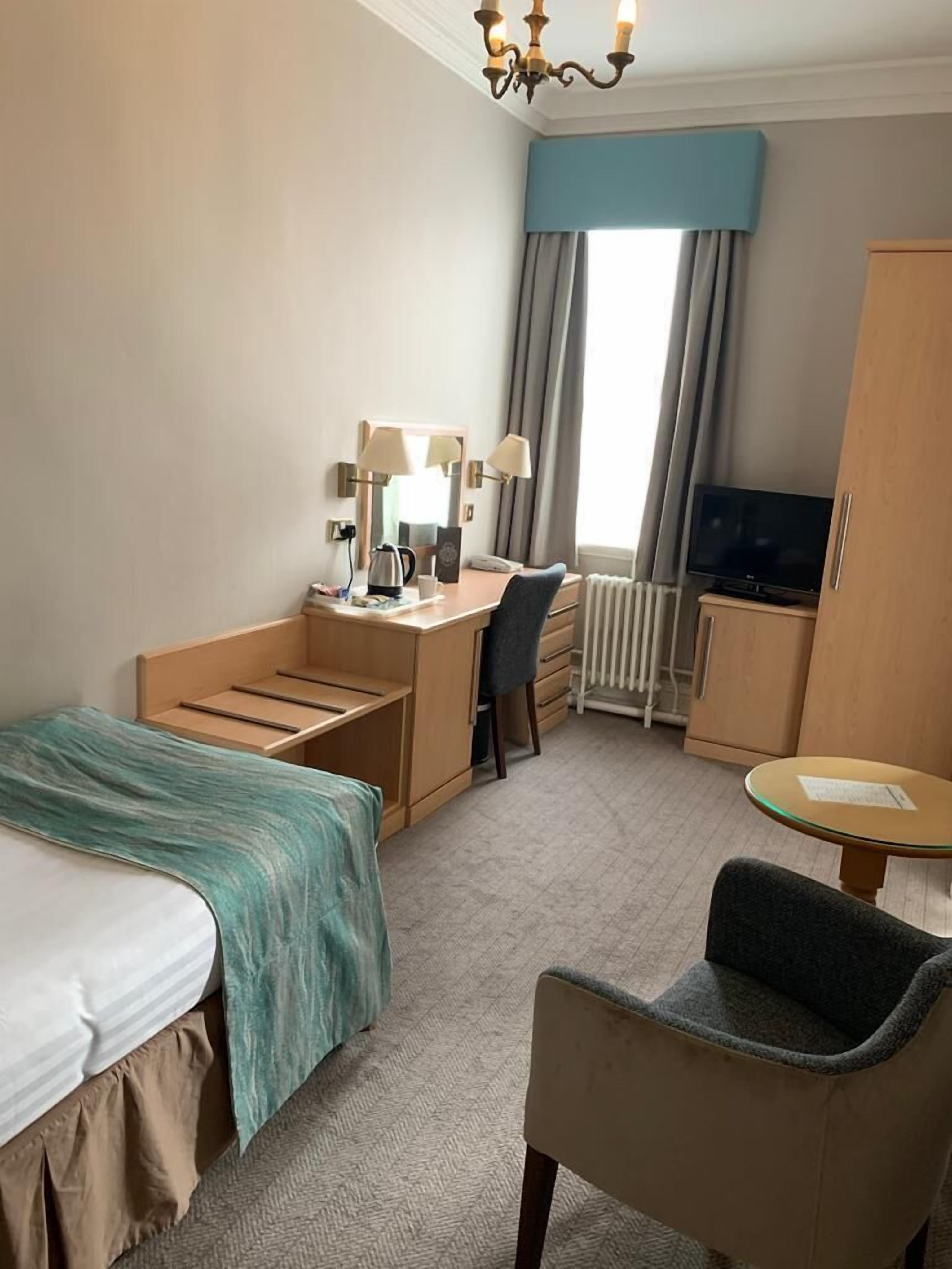A hotel room with a bed, desk, chair, TV, and a small table.