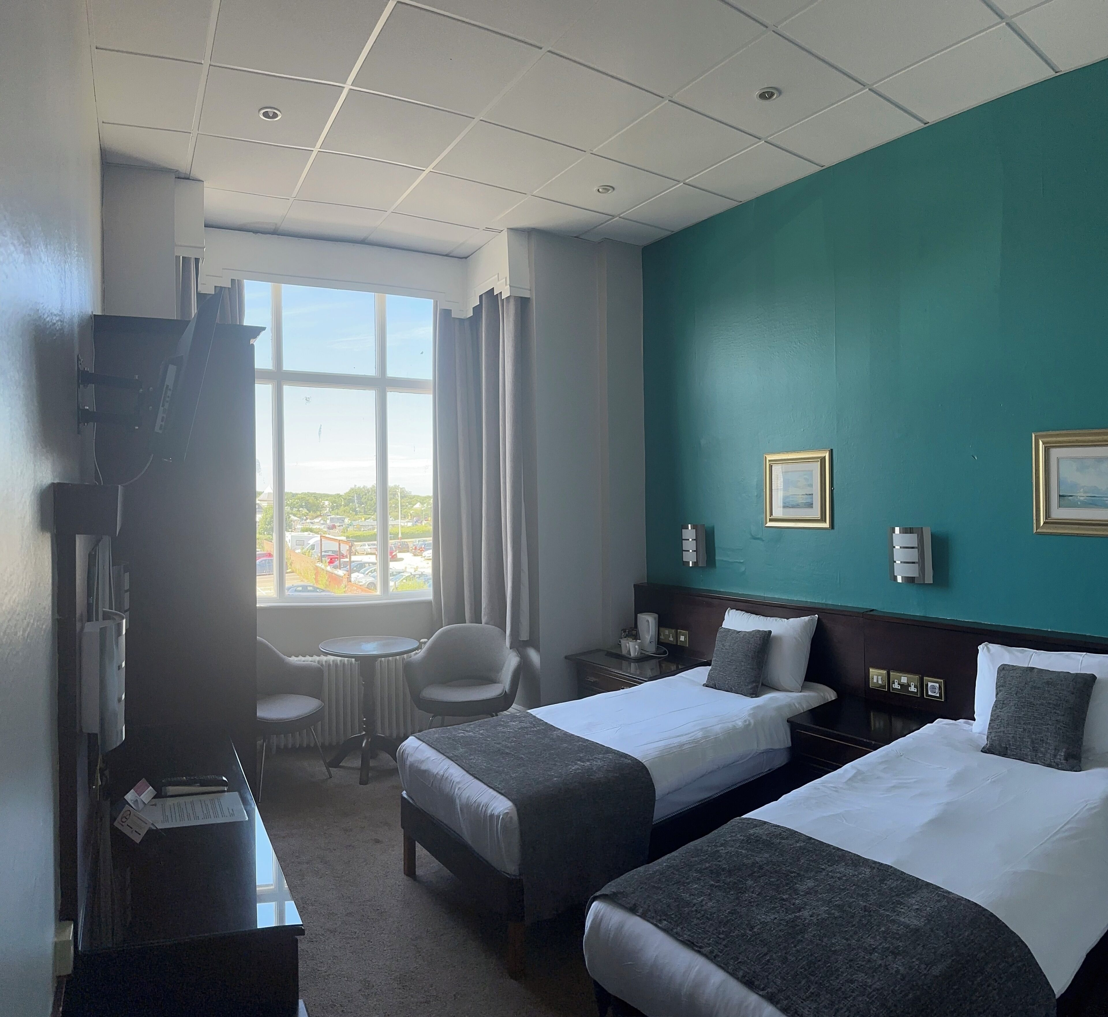A hotel room with two beds, a desk, a chair, a window with a view, and a television.