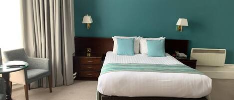 A hotel room with a large bed, two bedside tables, a chair, and a desk.