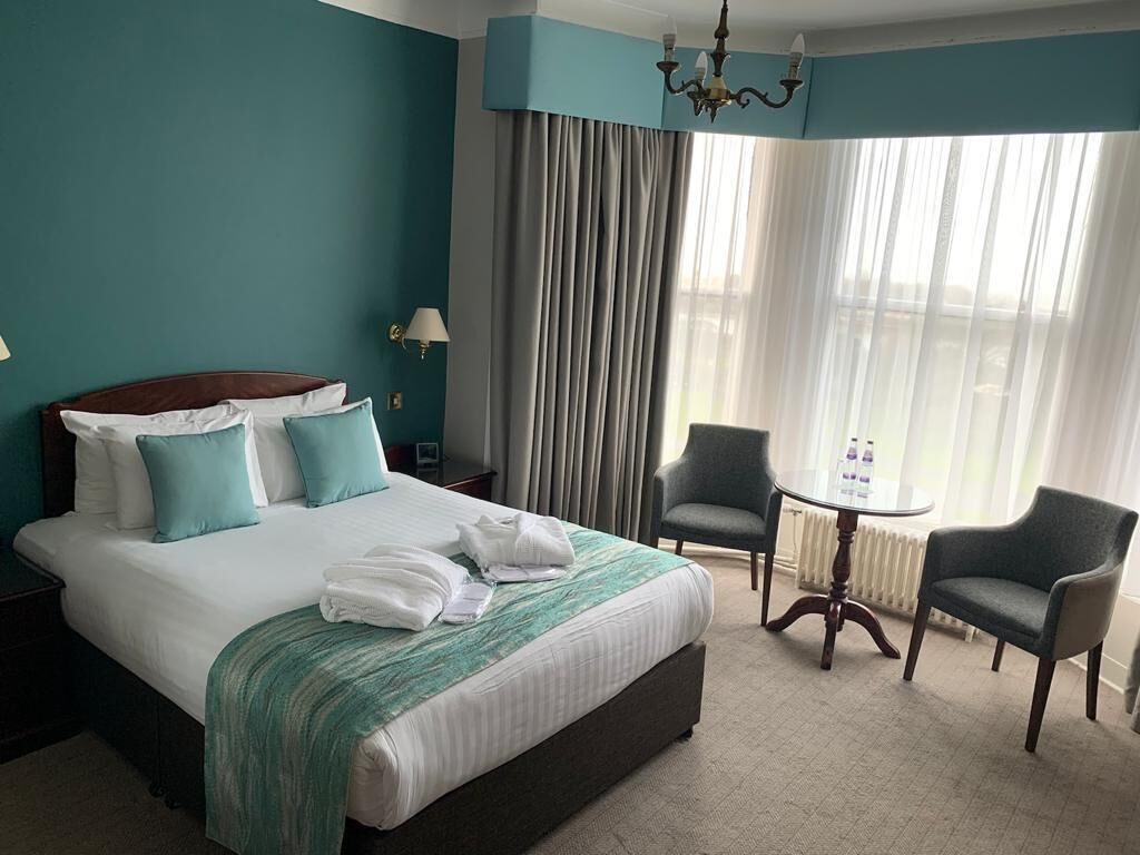 Habitación de hotel con una cama grande, dos sillones, una mesita y una ventana con cortinas.