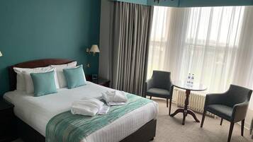 Habitación de hotel con una cama grande, dos sillones, una mesita y una ventana con cortinas.