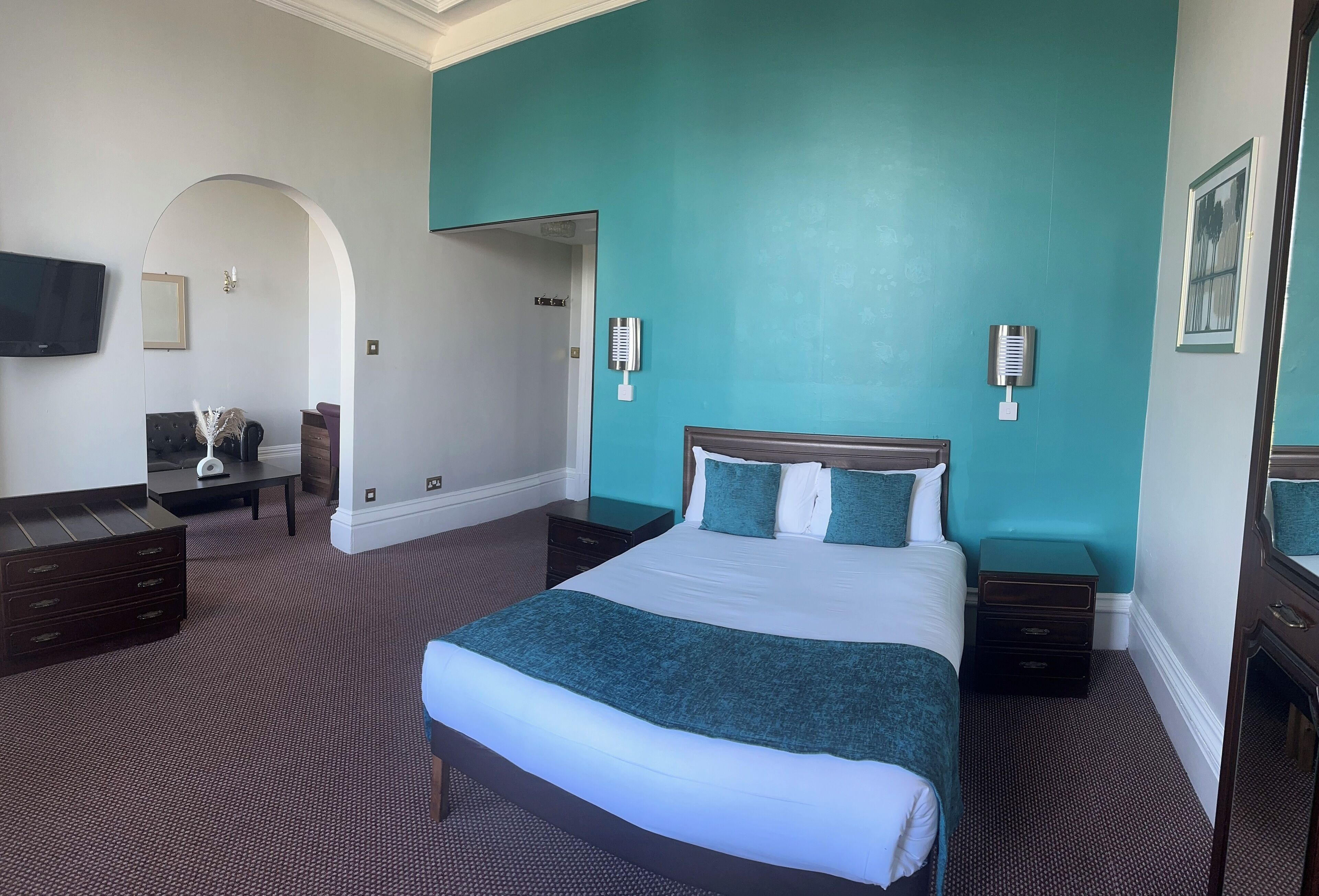 A hotel room with a large bed, a desk, a chair, and a TV on the wall.