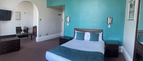 A hotel room with a large bed, a desk, a chair, and a TV on the wall.