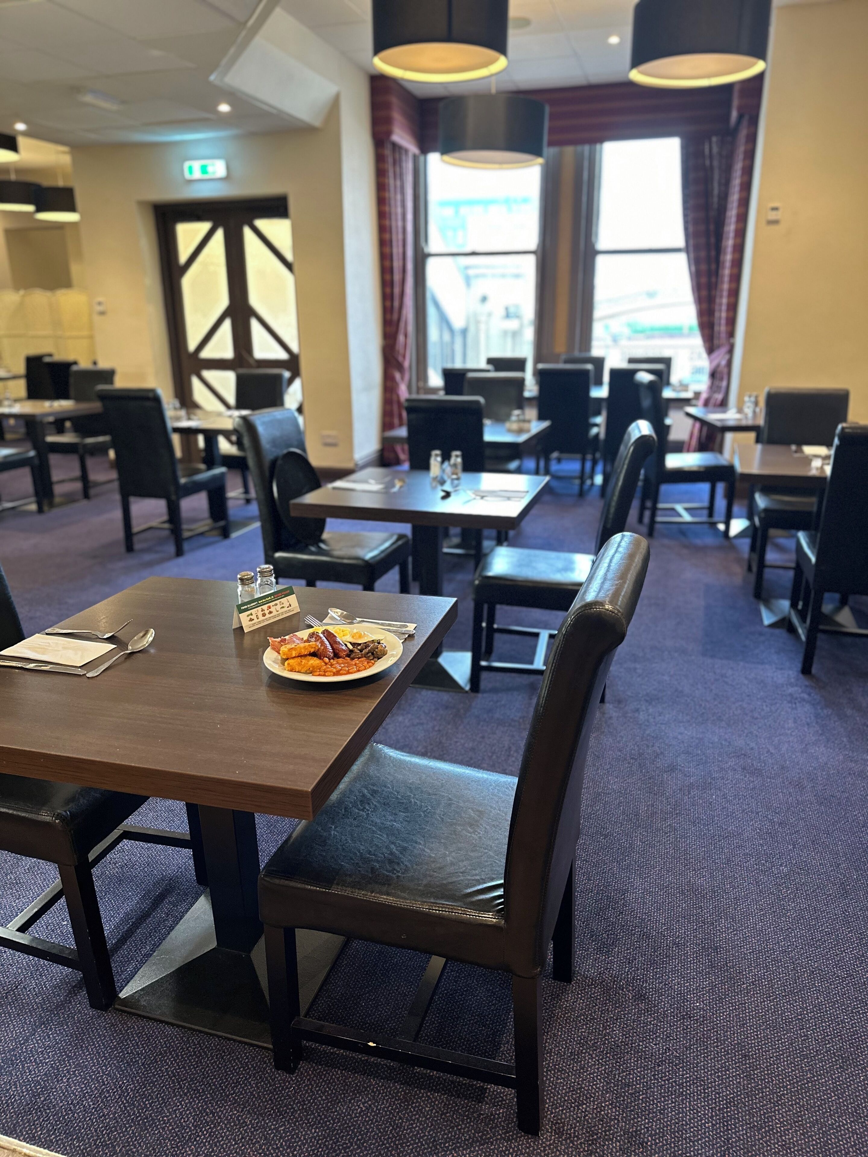 A restaurant with tables and chairs, a plate of food on one table, and a window with curtains in the background.