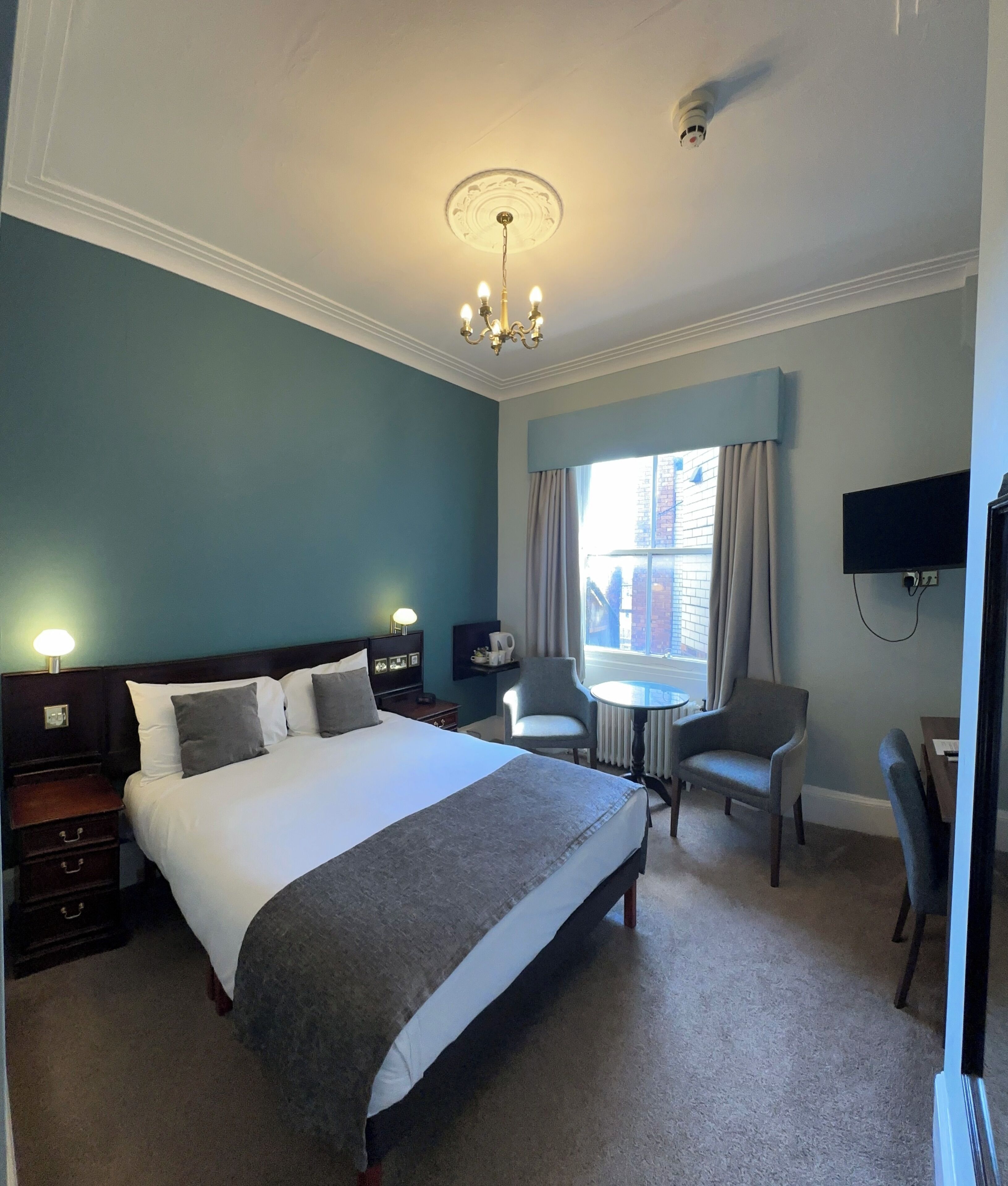 A hotel room with a large bed, a desk, a chair, a television, and a window with curtains.
