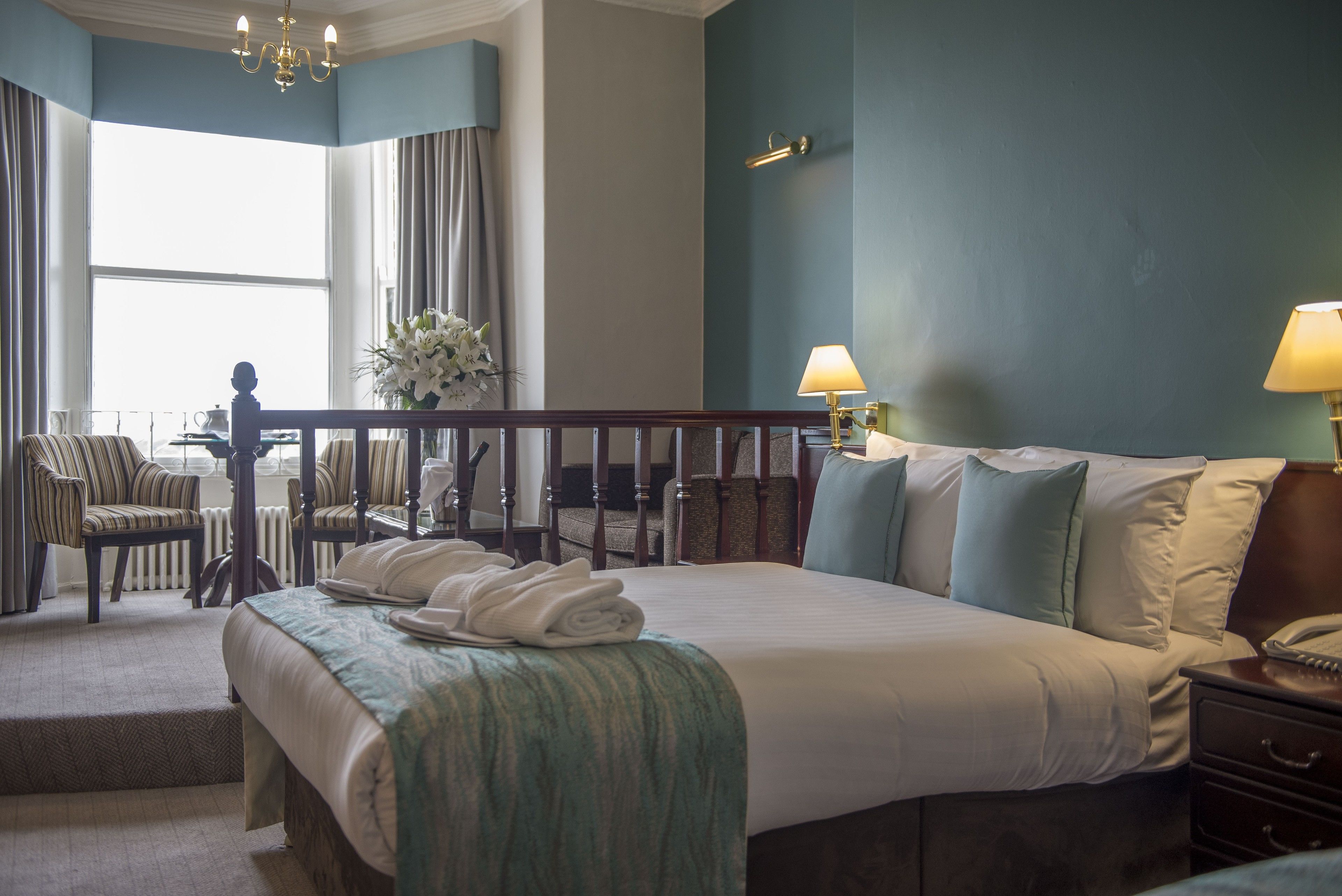 Habitación de hotel con una cama grande, una zona de estar con una silla, una mesita y vistas al exterior.