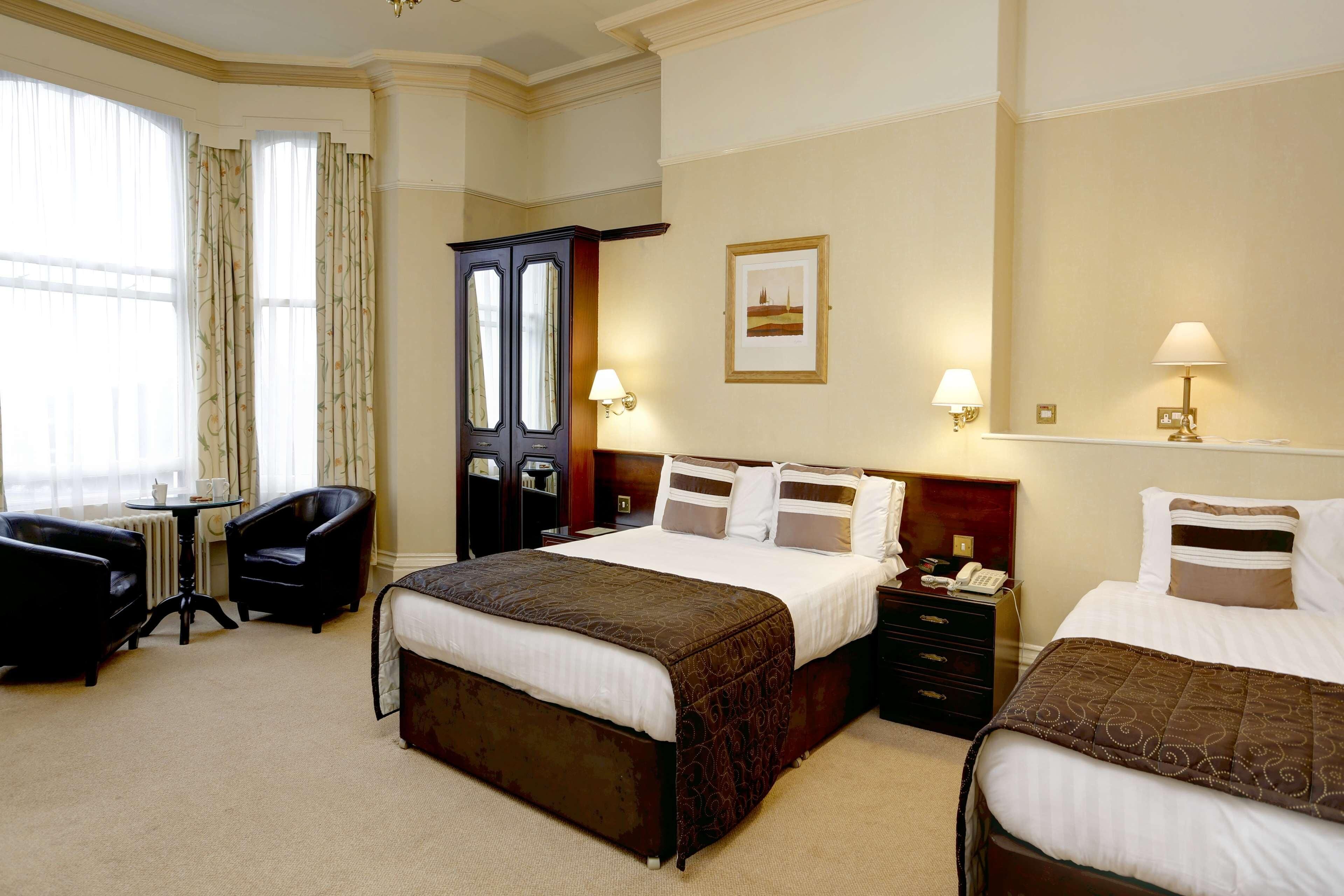A hotel room with two beds, a sitting area with a table and chairs, a wardrobe, and a framed picture on the wall.