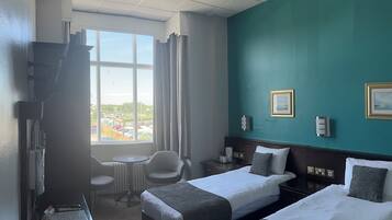 Habitación de hotel con dos camas, un escritorio, una silla, una ventana con vistas y un televisor.