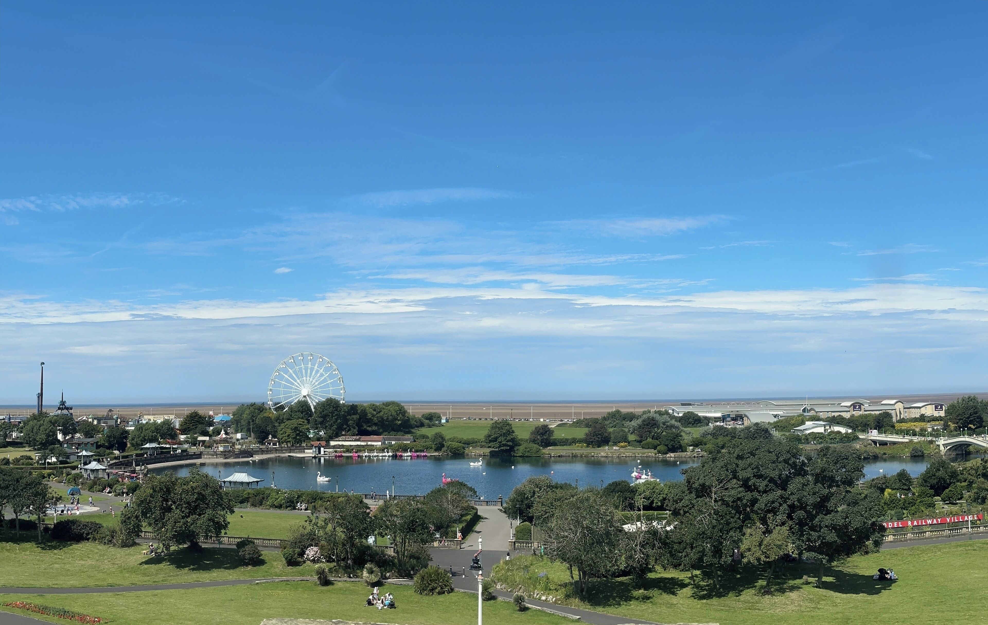 Un parc avec un lac, une grande roue et un panneau indiquant « DEL RAILWAY VILLAGE ».