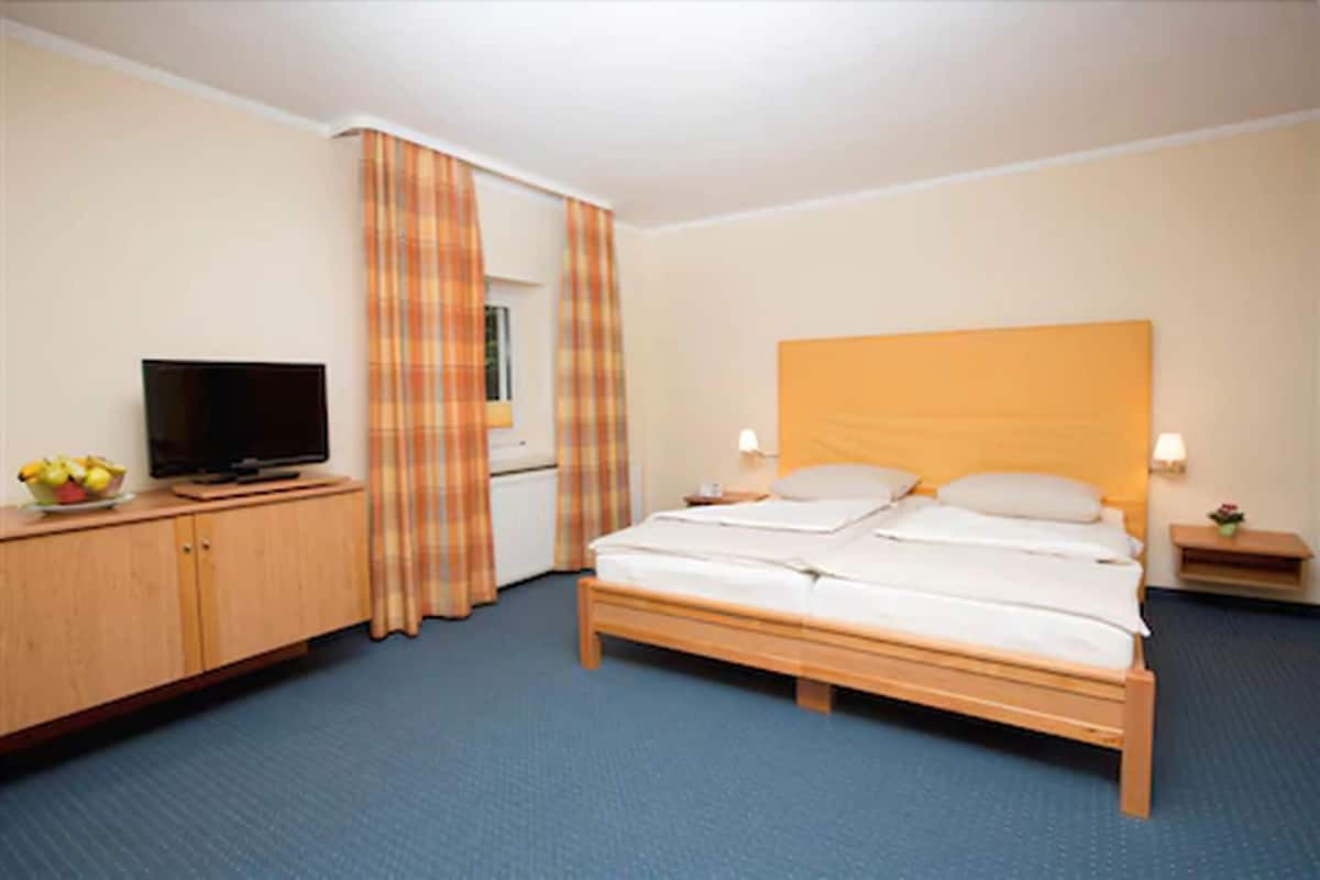 Une chambre d’hôtel avec un lit, un téléviseur posé sur une commode en bois et une petite table avec une lampe.