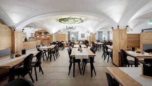 Un restaurante espacioso con techos altos abovedados, mesas y sillas de madera, y una lámpara central.