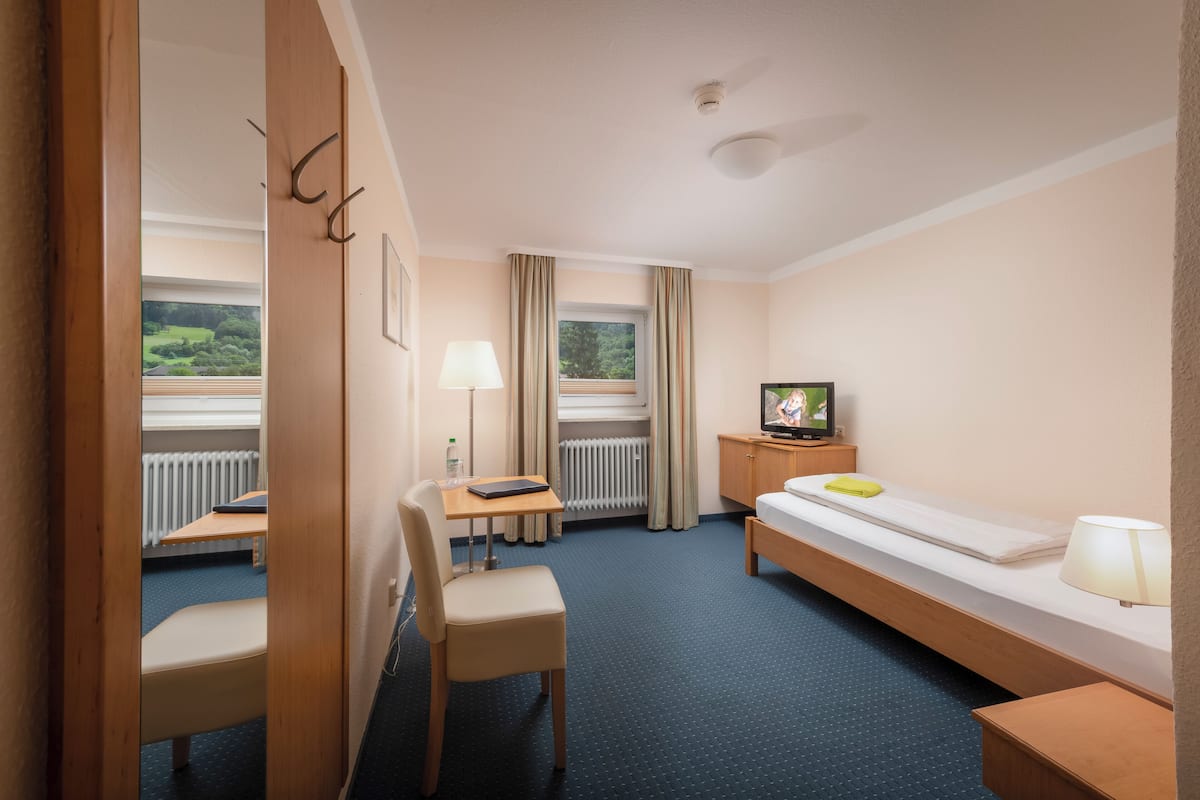 Une chambre d’hôtel avec un lit, un bureau et une chaise, une télévision et une fenêtre avec des rideaux.