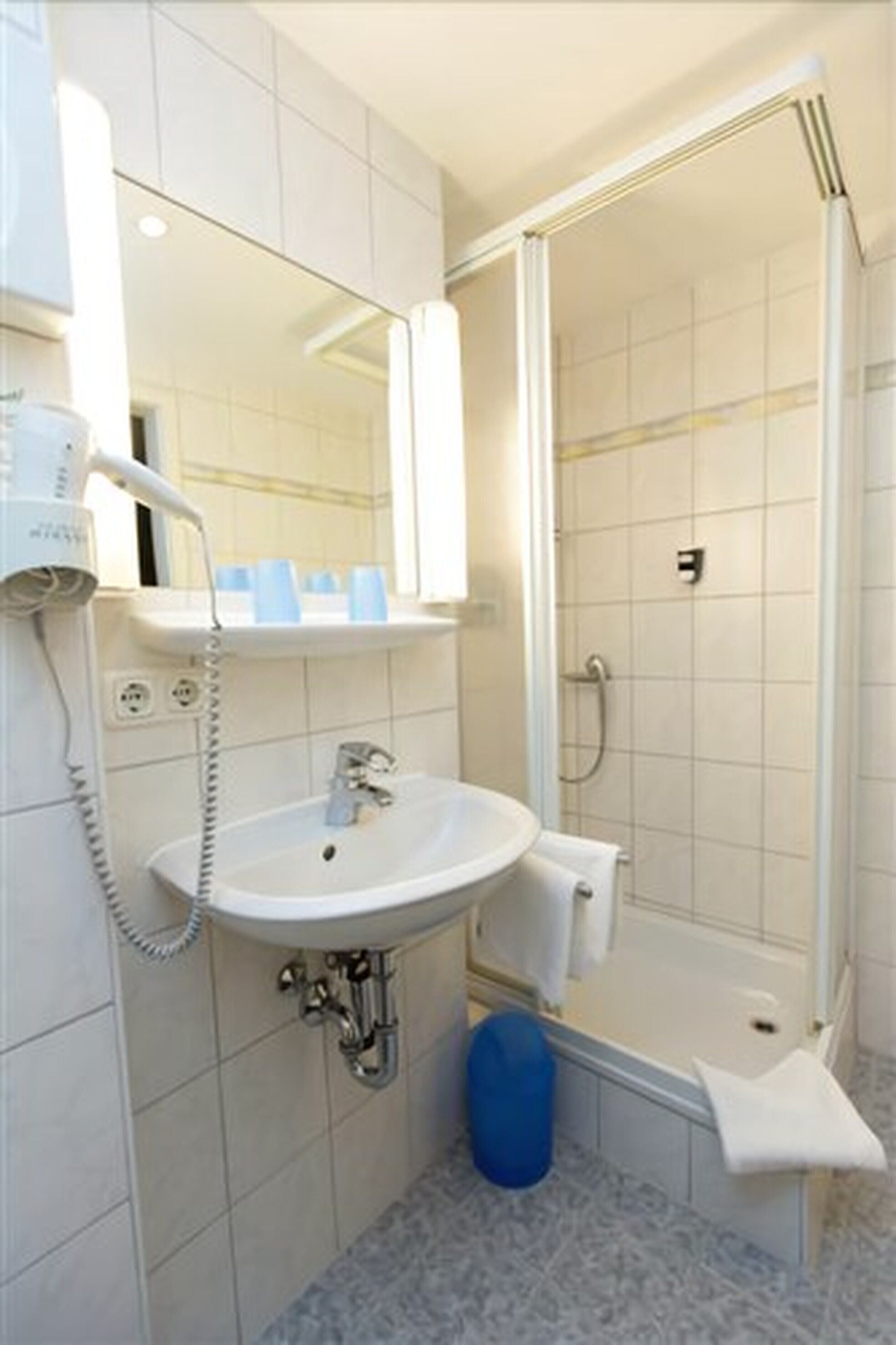 A bathroom with a white sink, a mirror, a hairdryer, and a shower.