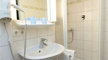 A bathroom with a white sink, a mirror, a hairdryer, and a shower.