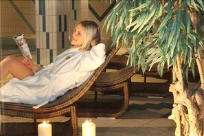 Une personne se détend sur un fauteuil en osier dans un espace intérieur bien éclairé, doté d’un sol carrelé et agrémenté d’une plante en pot à proximité.