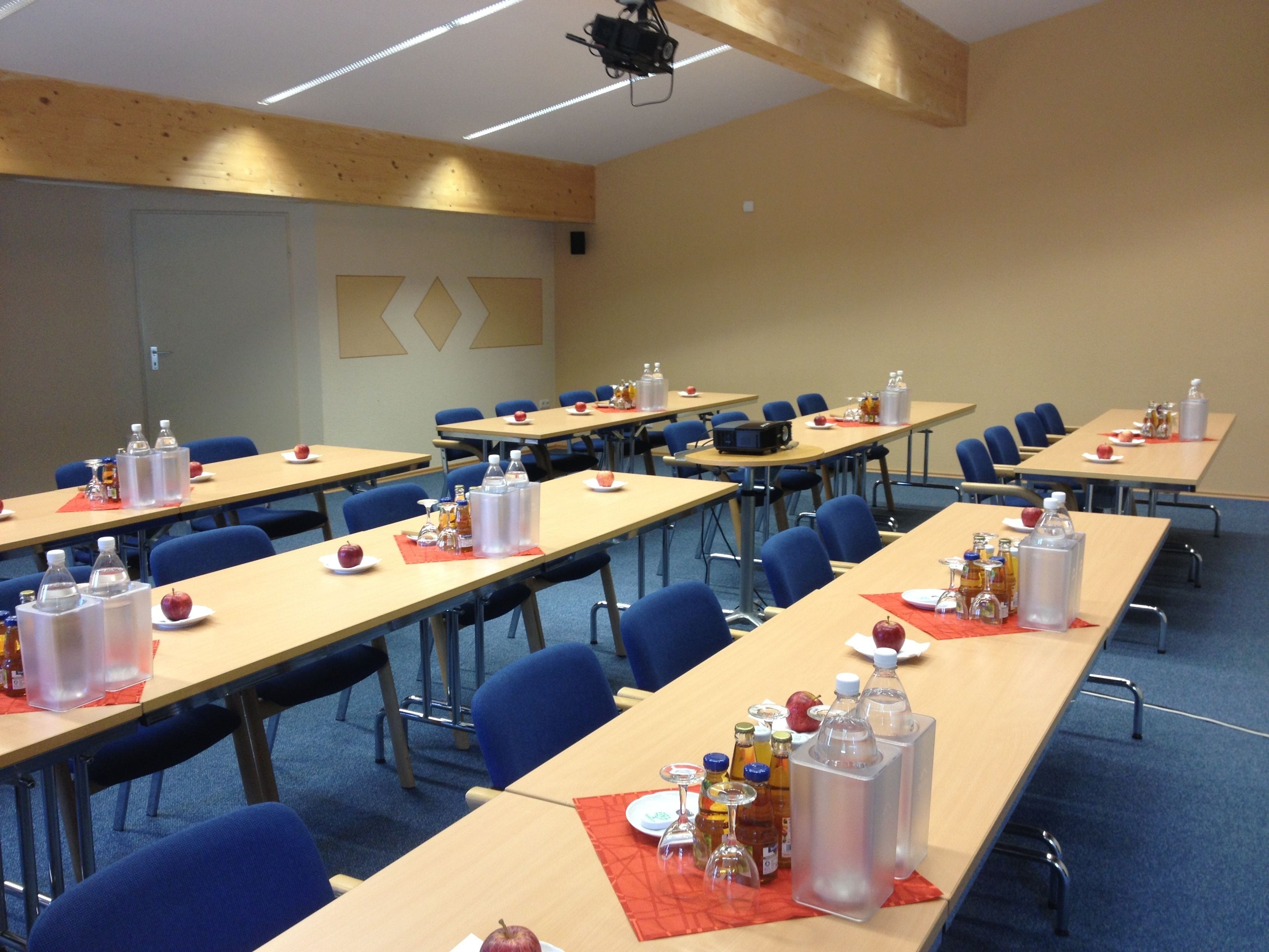A conference room with multiple tables, chairs, and various items like water bottles, apples, and glasses.