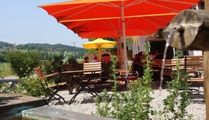 Een terras met houten banken en tafels, overdekt met rode en gele parasols, met uitzicht op een mooi landschap.