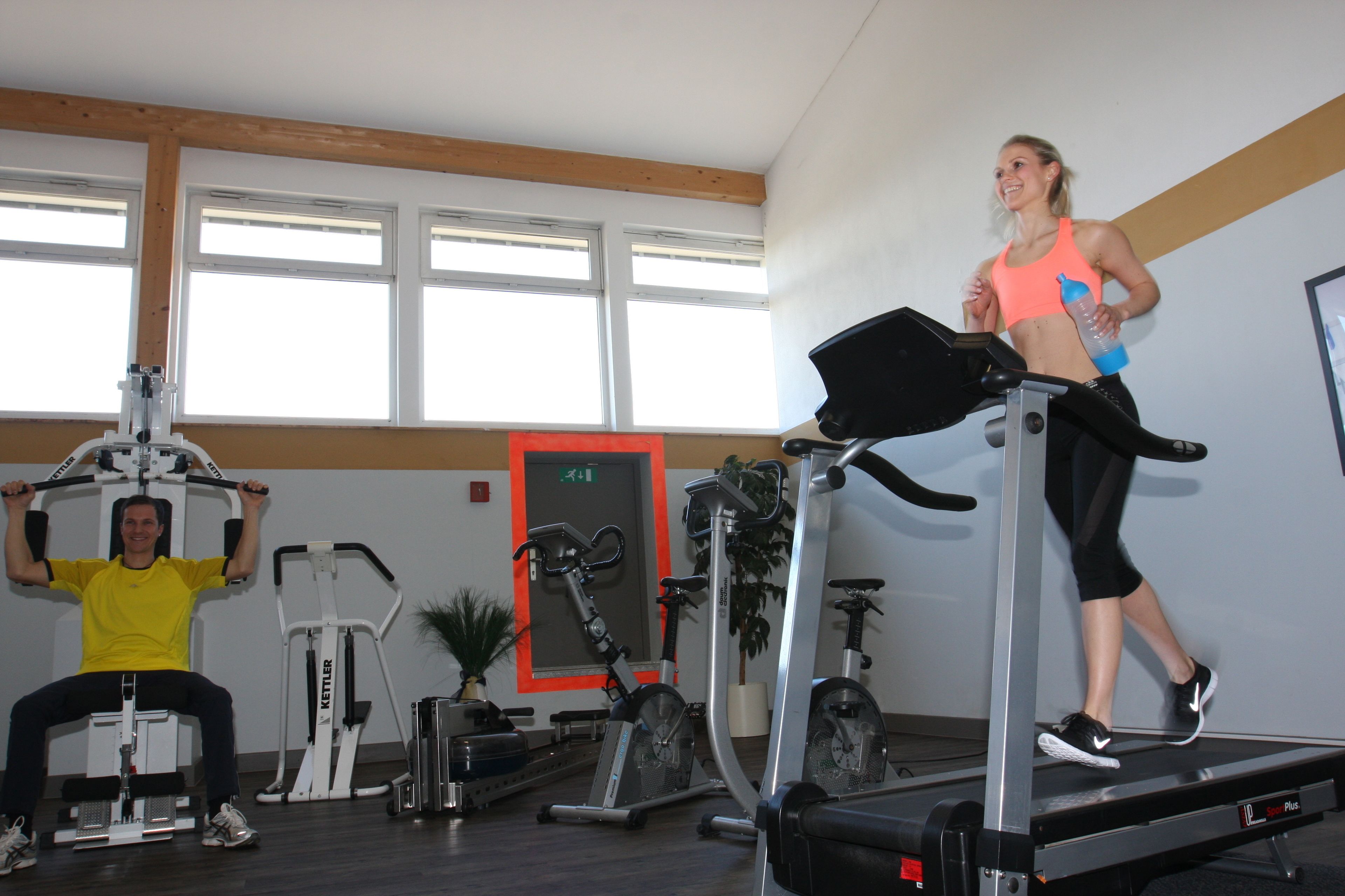 A gym with treadmills, a man using a leg press machine, and a woman on a treadmill.