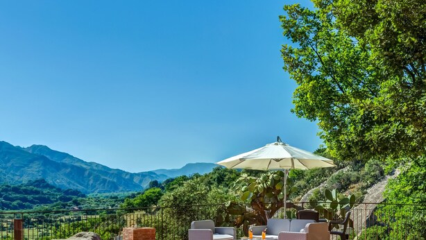 An outdoor patio with wicker furniture, a table, and a large umbrella, overlooking a mountainous landscape. - Il Poggio Luxury Country Resort (Graniti)