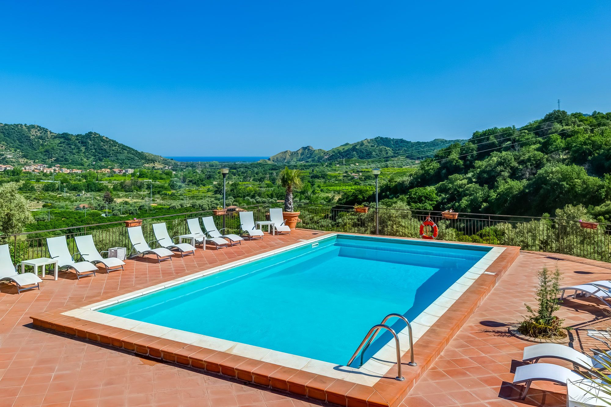 A rectangular pool with a tiled edge, surrounded by white lounge chairs and a metal ladder.