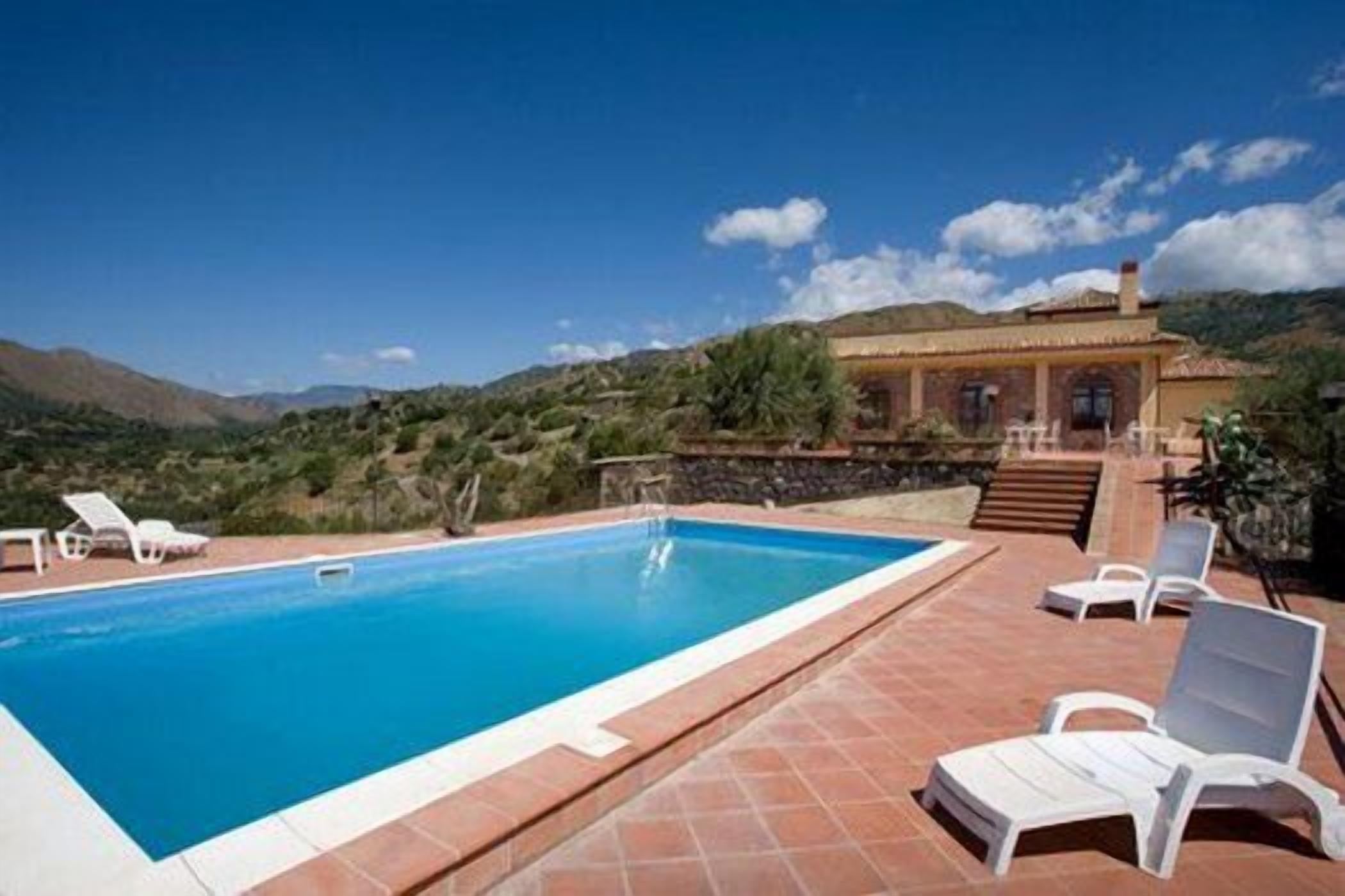 Une piscine entourée de chaises longues blanches, avec un bâtiment en pierre en arrière-plan.