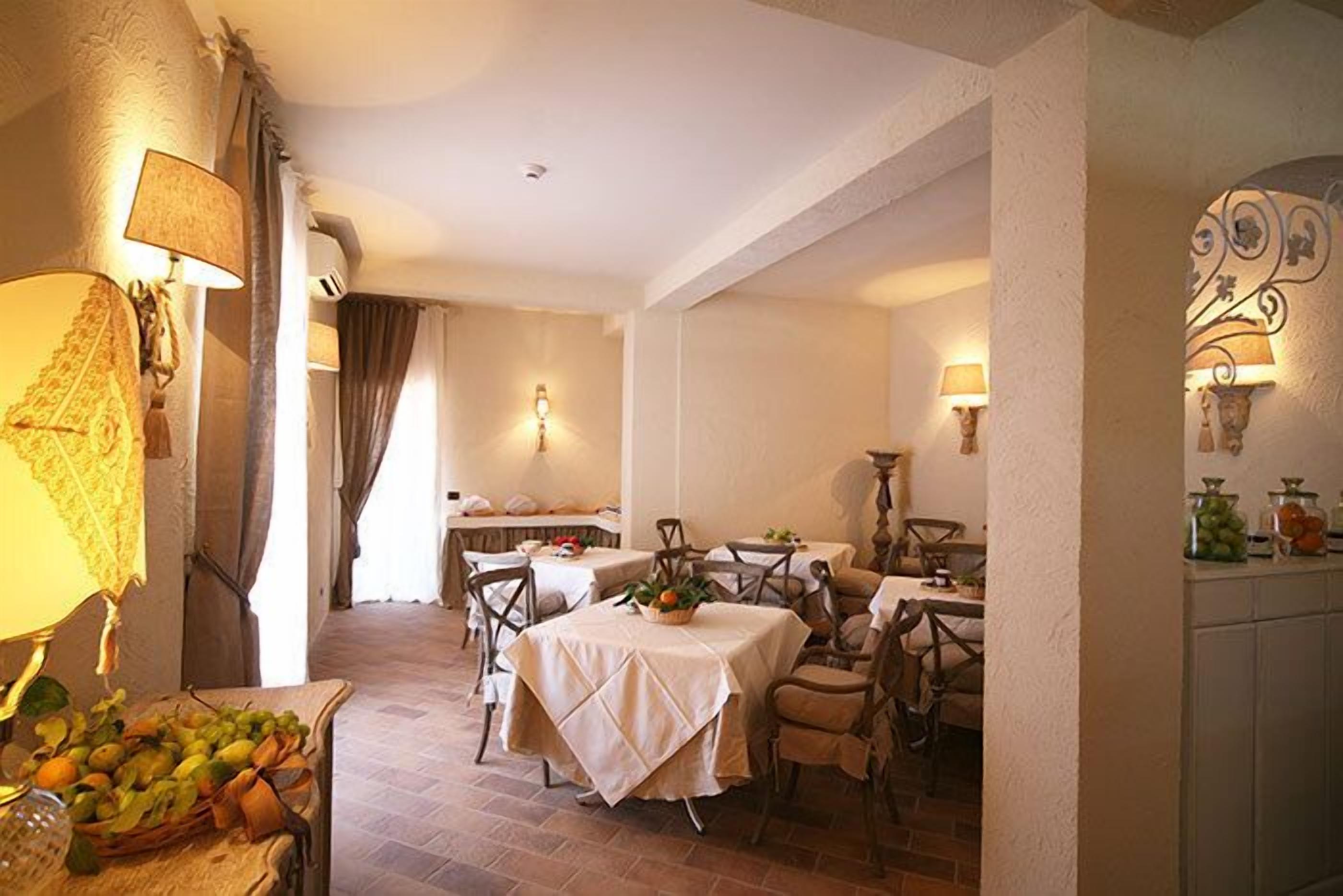 A dining area with tables and chairs, a buffet table with fruits, and wall-mounted lamps.