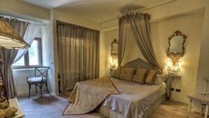 A bedroom with a four-poster bed, a chair, a bedside table with a lamp, and a window with curtains. - Il Poggio Luxury Country Resort (Graniti)