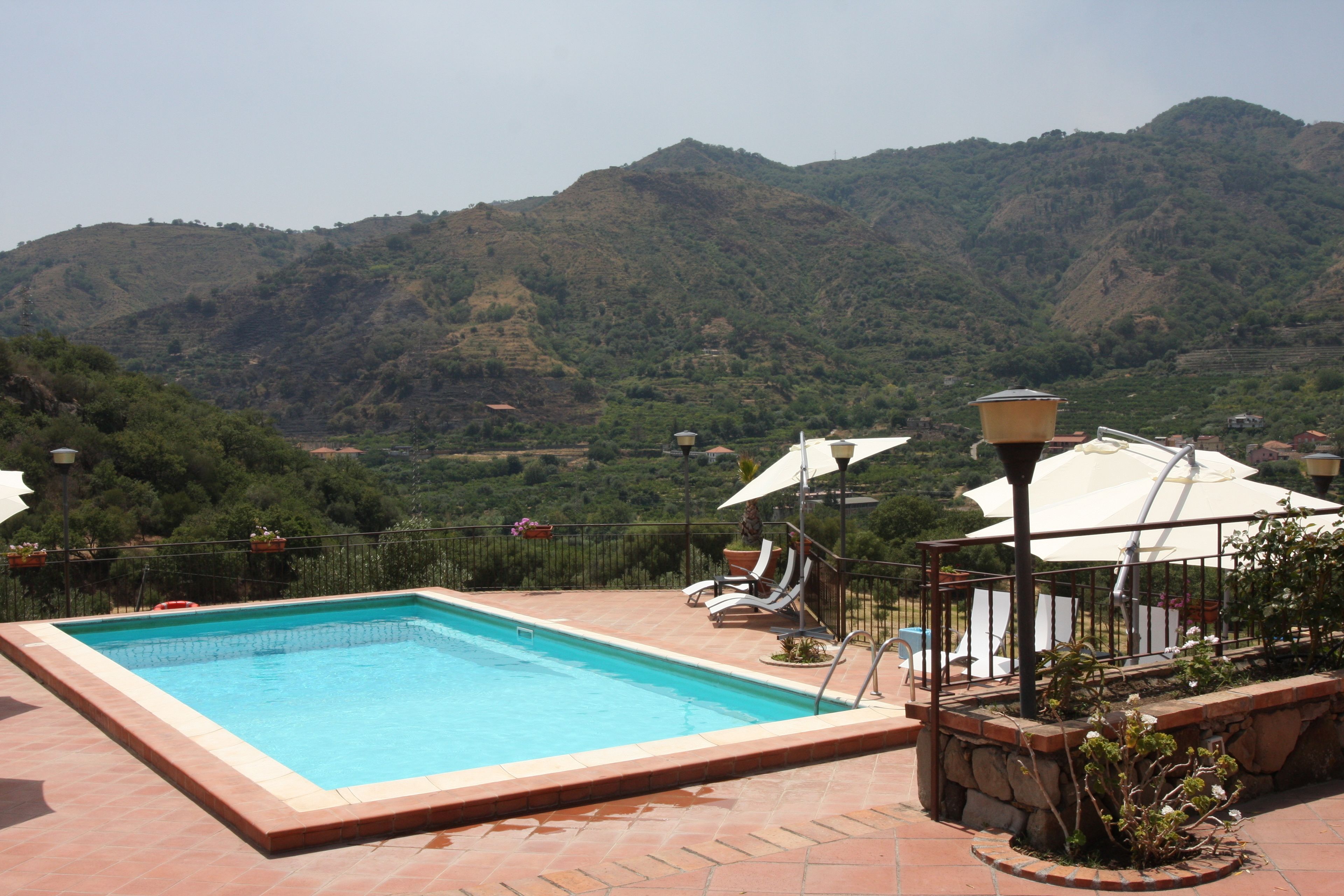A swimming pool with a view of mountains, outdoor seating, and umbrellas.
