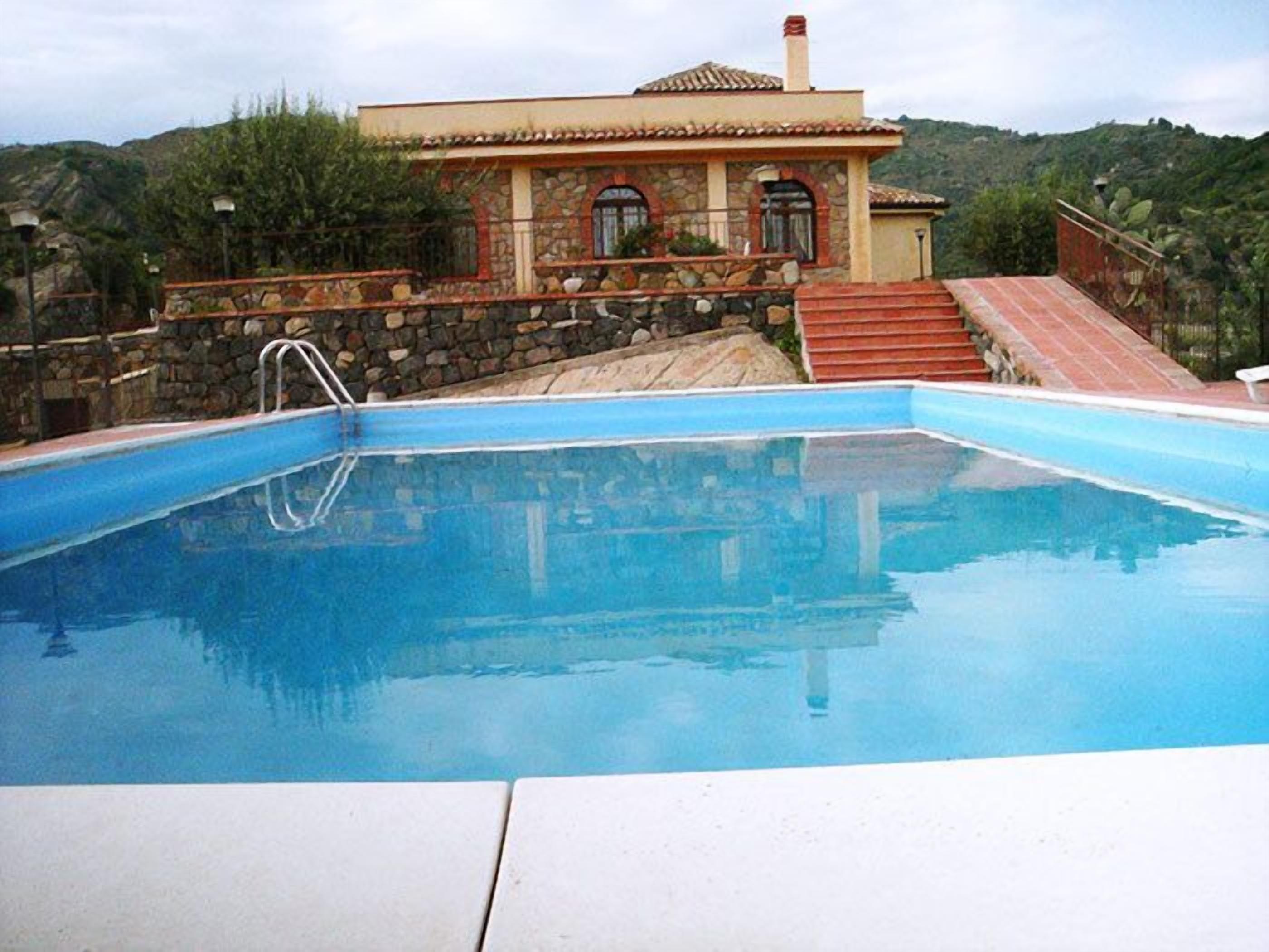 A swimming pool with a stone wall and a house in the background.