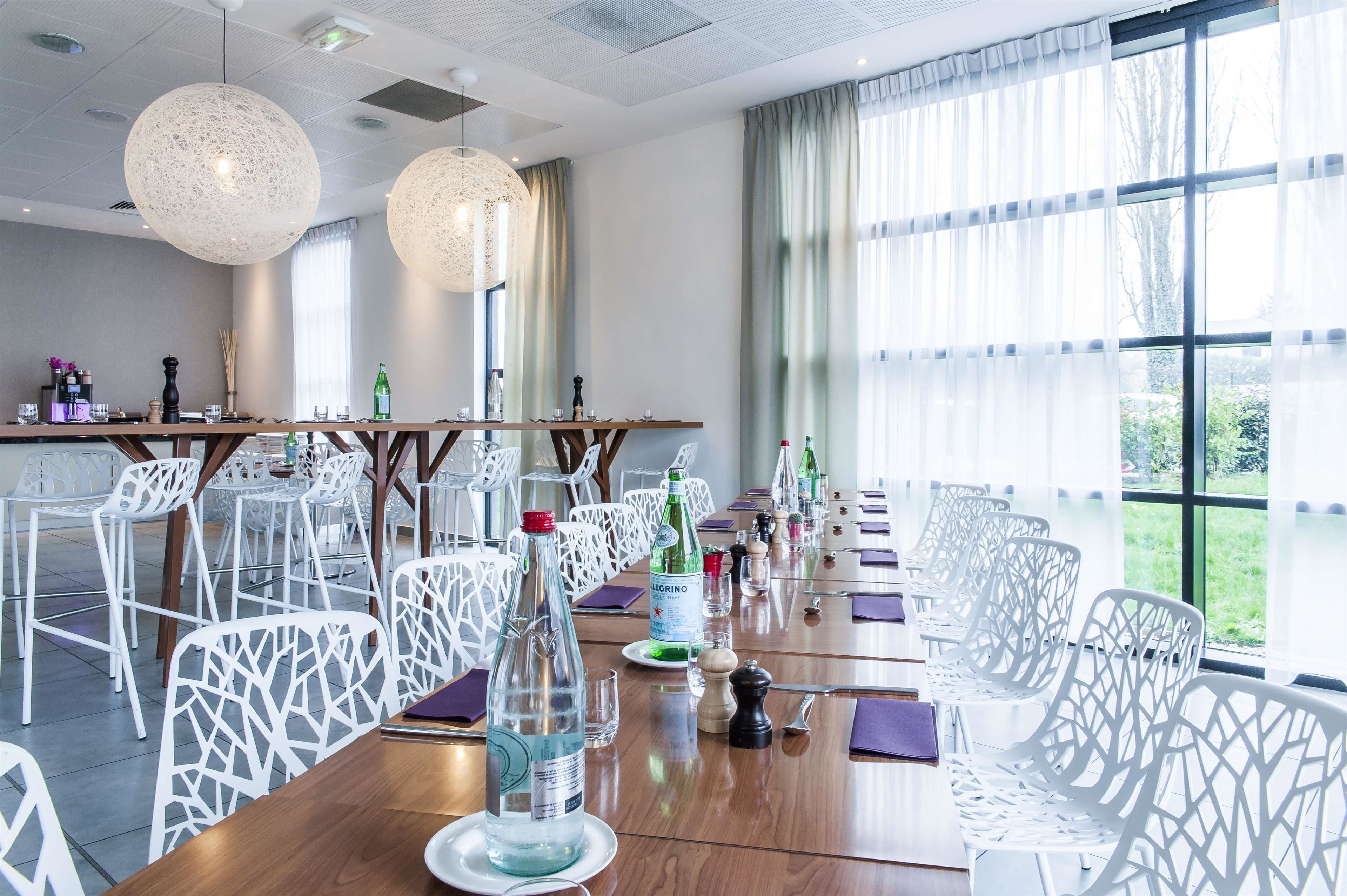A dining area with white chairs, a long wooden table, and hanging spherical light fixtures.