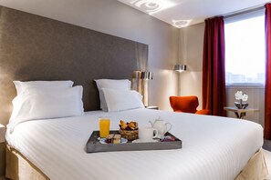 A hotel room with a neatly made bed, a tray with breakfast items, a red chair, and a view of the city through the window. - Best Western Plus Paris Velizy (Velizy-Villacoublay)