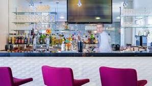 Un espace bar avec un comptoir, des étagères remplies de bouteilles et de verres, et un écran de télévision.