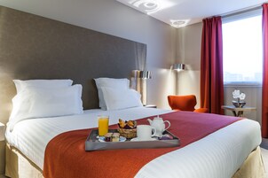 Habitación de hotel con una cama grande, una bandeja con alimentos para el desayuno, una ventana con cortinas y una pequeña mesa con una lámpara.