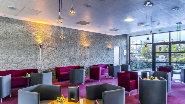 Un salon moderne avec des murs en pierre, des sièges rouges et gris et des luminaires suspendus.