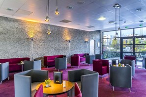Un salon moderne avec des murs en pierre, des sièges rouges et gris et des luminaires suspendus.