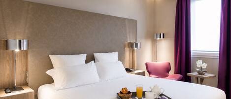 A hotel room with a large bed, bedside lamps, a pink chair, a small table with a vase of flowers, and a tray with breakfast items.