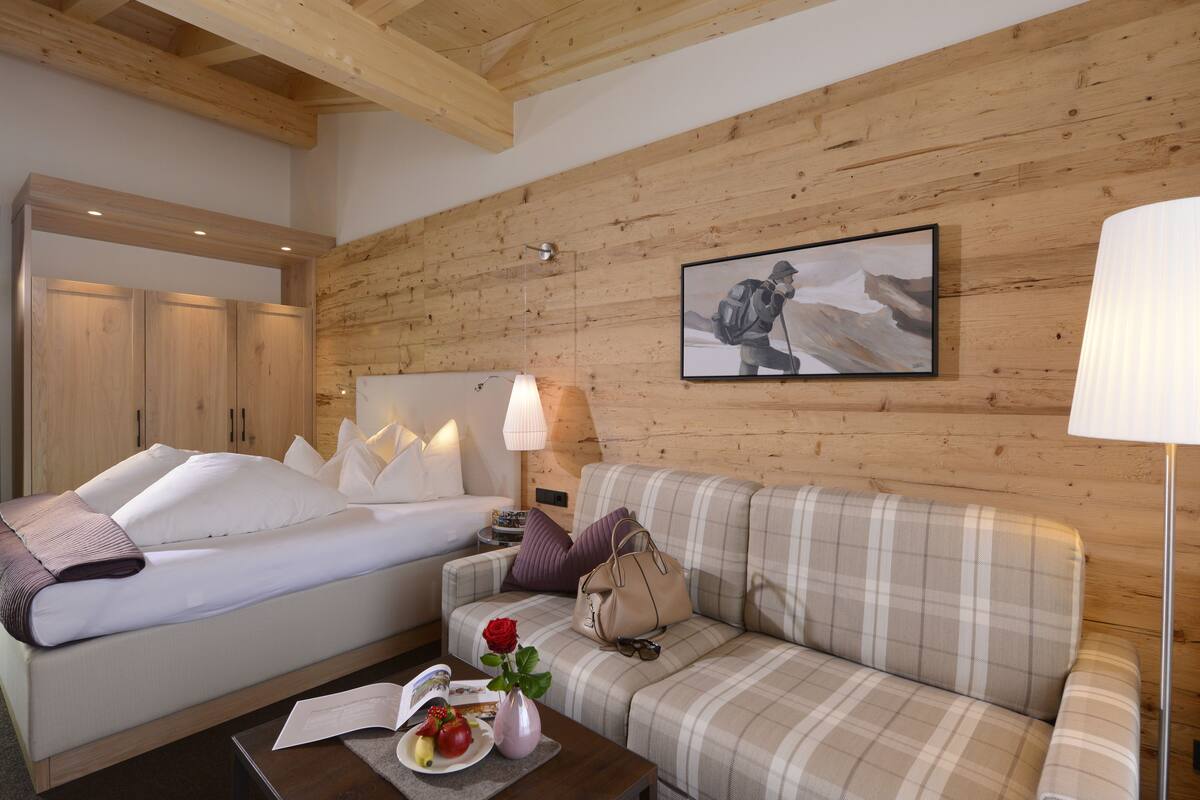 Une chambre d’hôtel avec un lit, un canapé, une table ornée d’un vase et d’une rose, et un tableau accroché au mur.