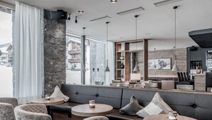 Un interior moderno con una pared de acento de piedra, zonas de estar con mesas redondas y una barra con un espejo grande y estanterías.