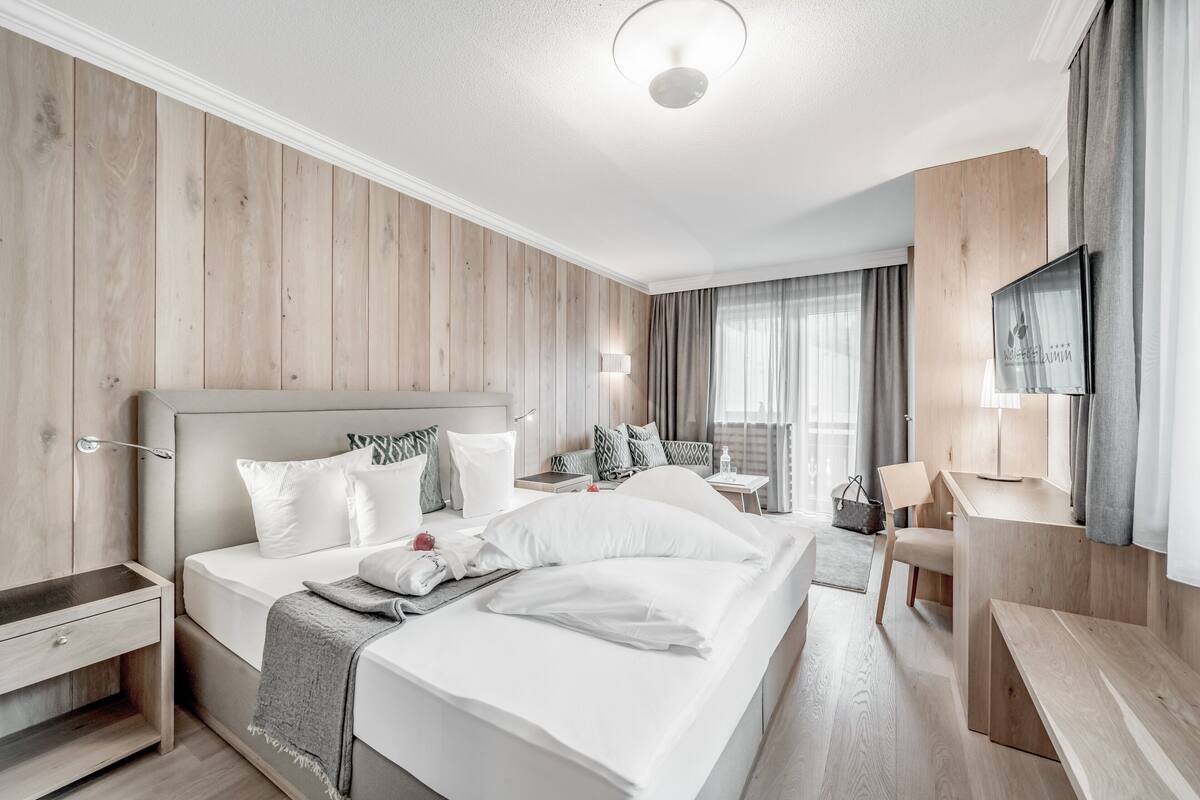 Une chambre d’hôtel moderne dotée d’un grand lit, de tables de chevet, d’un bureau, d’une chaise, d’une télévision et d’une fenêtre avec des rideaux.