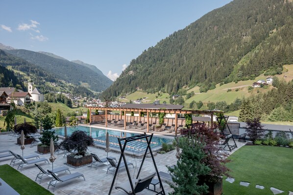 A pool area with lounge chairs and umbrellas, surrounded by a mountainous landscape and a church.