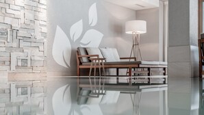 Un interior moderno con un sofá frente a una pared texturizada, una lámpara de pie y una mesa de vidrio reflectante.