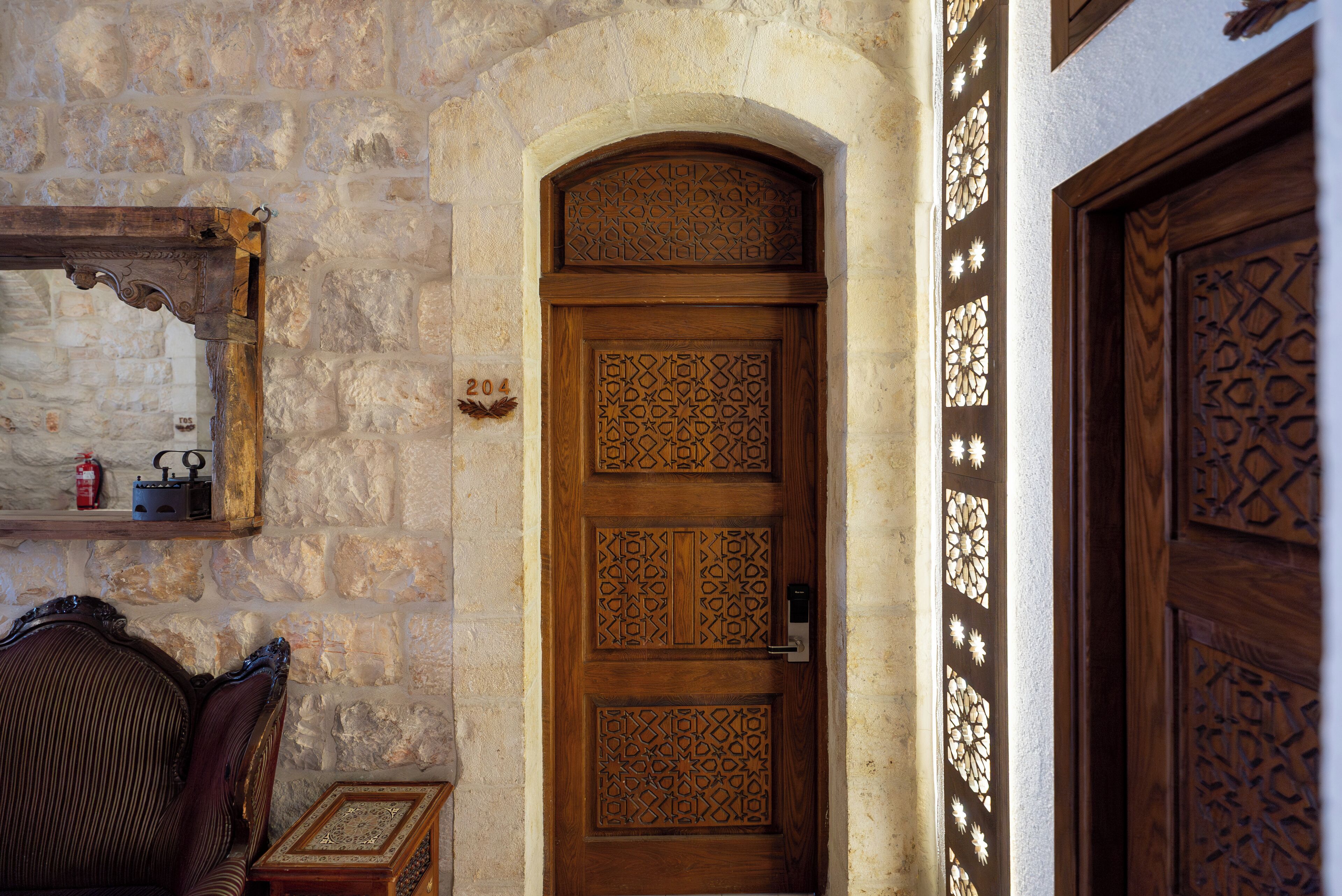 A wooden door with intricate carvings, a stone wall, and a small wooden table with a chair.