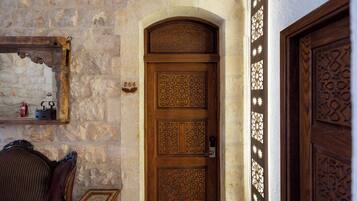 A wooden door with intricate carvings, a stone wall, and a small wooden table with a chair.
