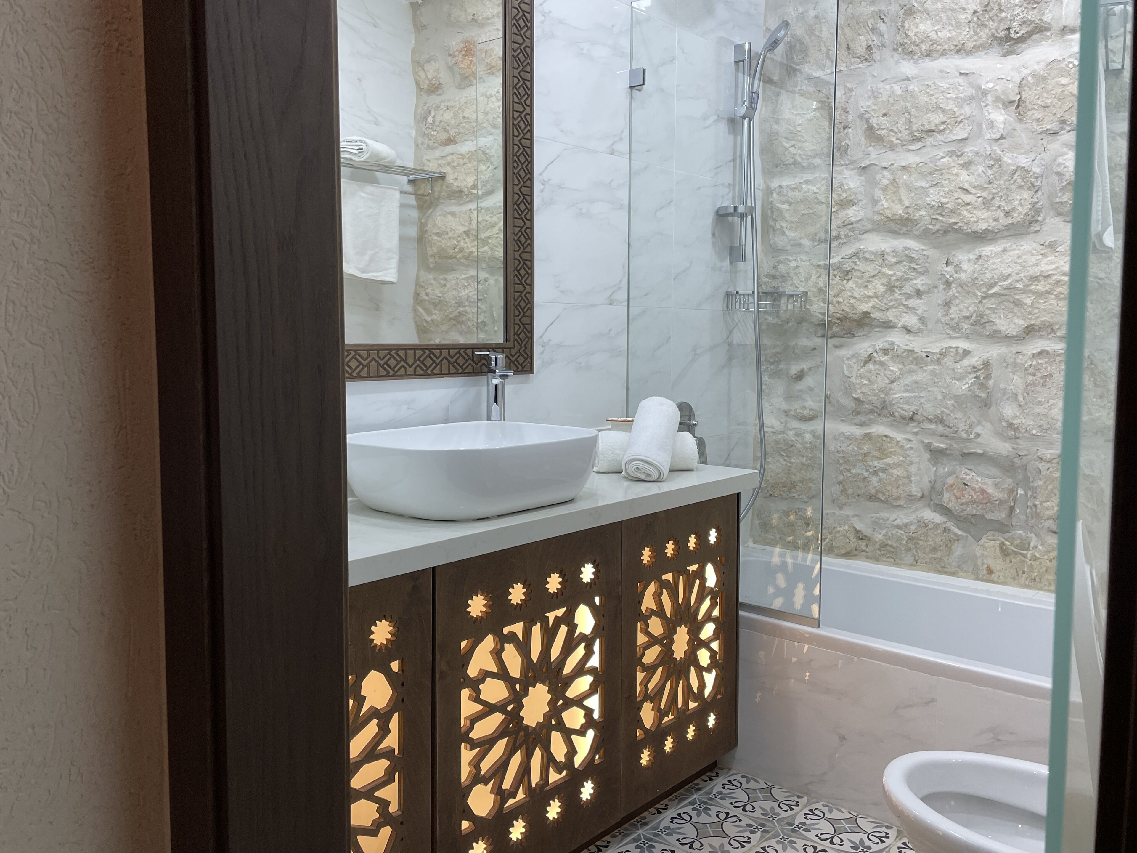 Un bagno moderno con un lavabo bianco grande, una cabina doccia in vetro e una parete di pietra.