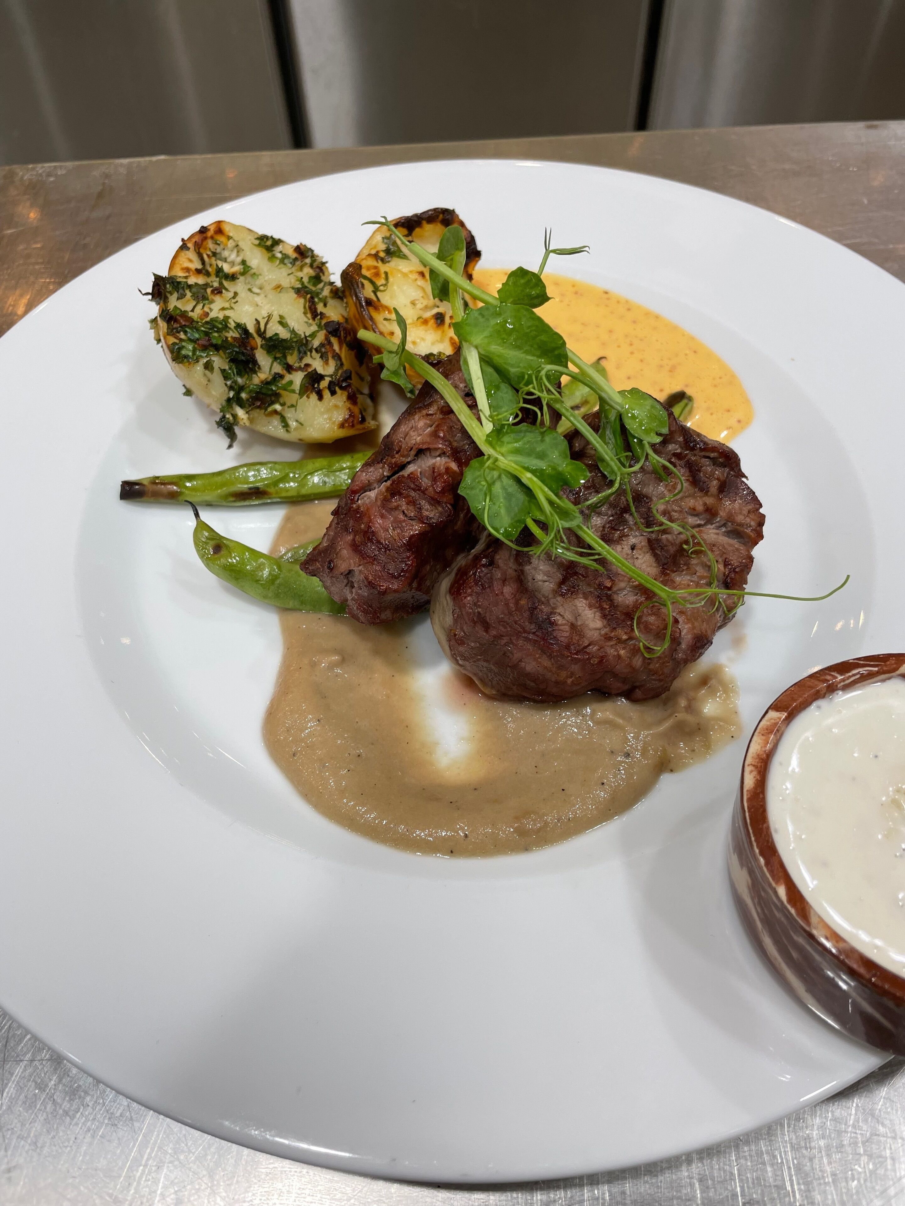 Une assiette de nourriture comprenant de la viande grillée, des pommes de terre rôties, des asperges et une sauce crémeuse.