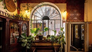 Een knus interieur met een groot rondboogvenster, houten meubels en diverse potplanten.