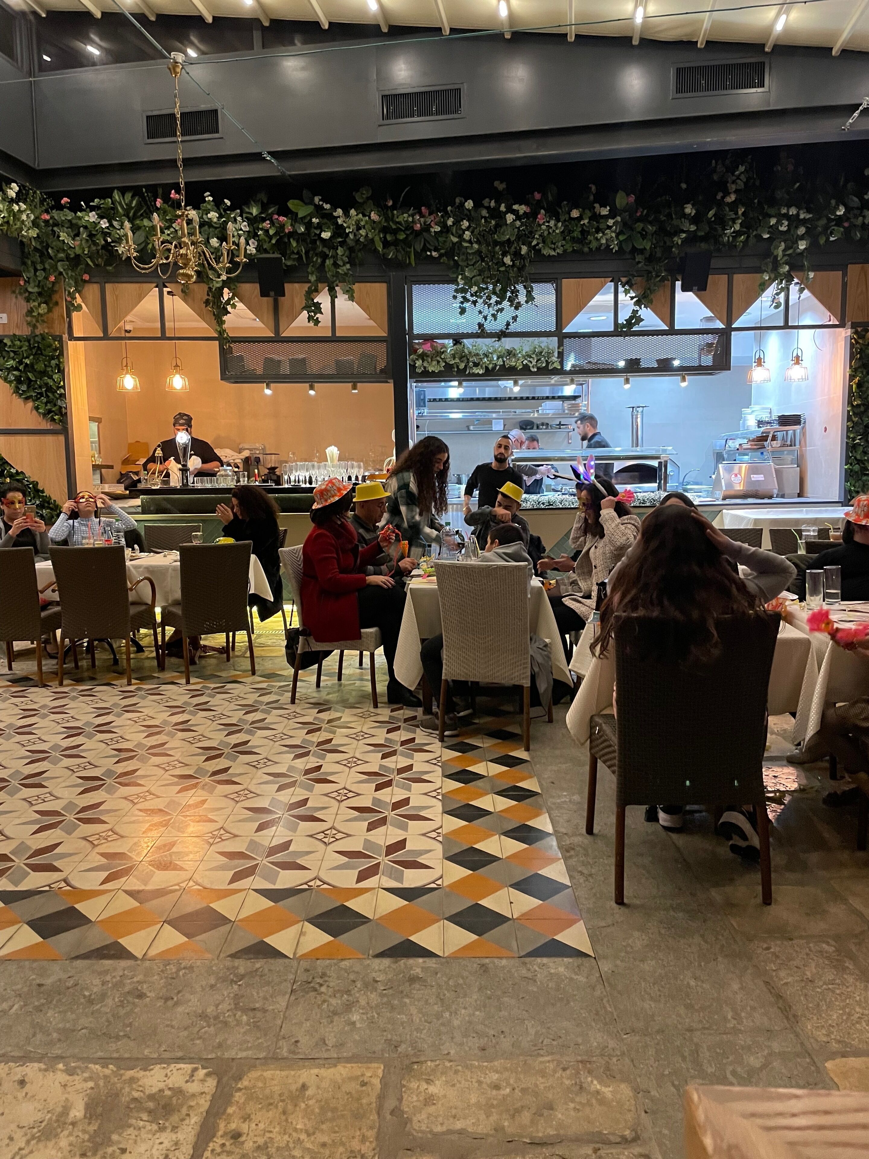 Un restaurant avec un sol carrelé à motifs, des plantes d’intérieur et un bar situé au fond de la salle.